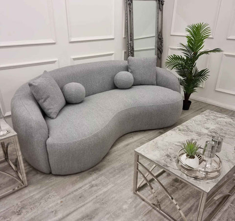 Luxury grey Wave bouclé sofa with a sculptural curved silhouette, premium textured upholstery, deep foam cushions, and modern designer styling in a contemporary UK living room.