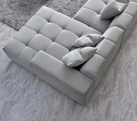  grey bouclé right-hand corner sofa with modular L-shaped design, block-stitched cushions, and five matching scatter cushions in a contemporary living room.
